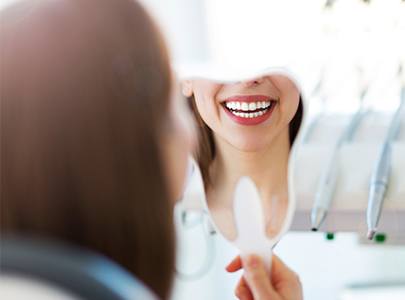 Woman looking at smile in mirror after smile makeover