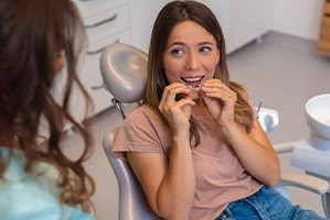 Woman smiling while holding clear aligners in treatment chair