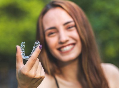 Woman with long brown hair holding a clear aligner outside