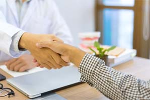 Dentist and patient shaking hands over a desk