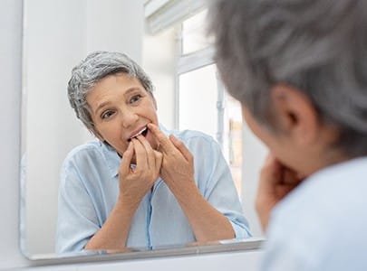 Woman flossing teeth to care for her dental crowns