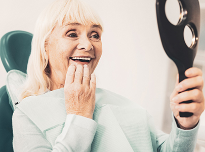 An elderly woman admiring her dentures in a hand mirror