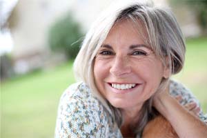 Older woman smiling in a field with dental implants in Cary, NC