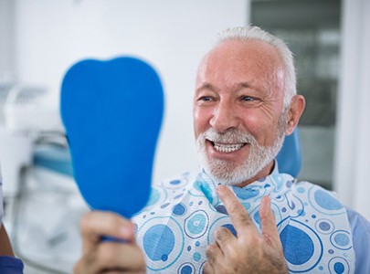 senior man admiring his smile after getting dental implants in Cary