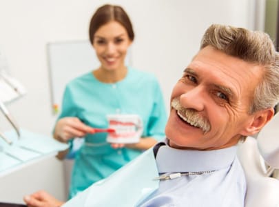 older man smiling in dental chair with hygienist