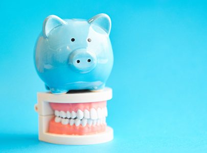 Piggy bank atop model teeth representing the cost of Invisalign in Cary