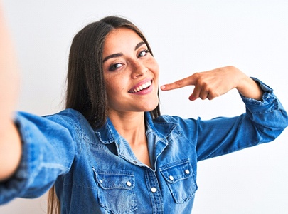 Woman pointing to her teeth after smile makeover in Cary