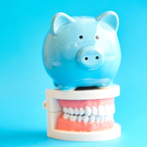 Blue piggy bank atop model teeth representing the cost of veneers in Cary
