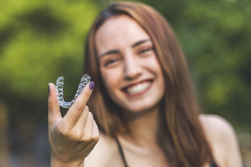 person smiling while holding Invisalign aligner