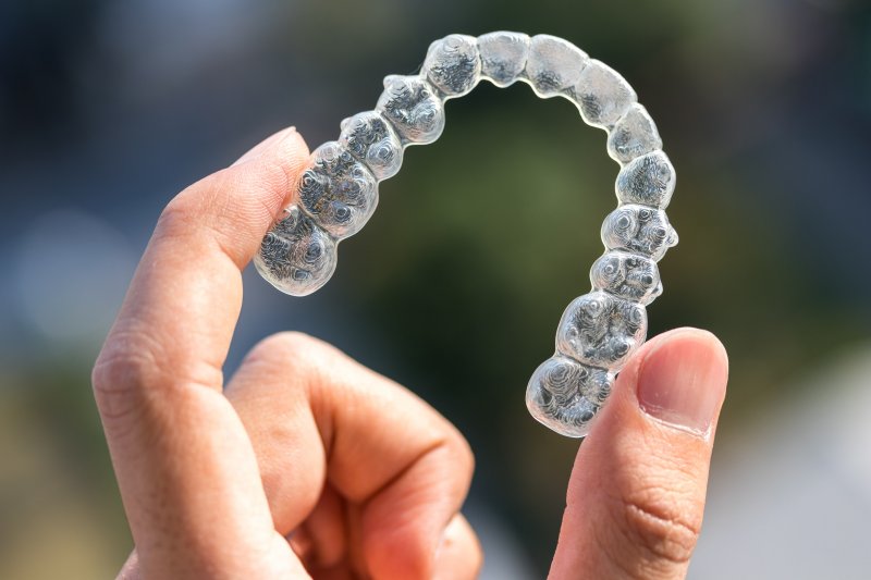 Left hand holding Invisalign up with index finger and thumb
