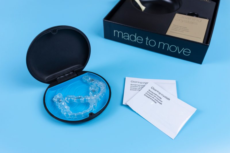 A pair of Invisalign aligners next to packets of cleaning crystals