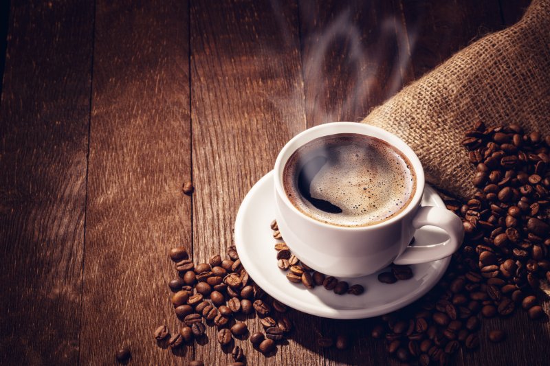 A steaming cup of coffee surrounded by coffee beans